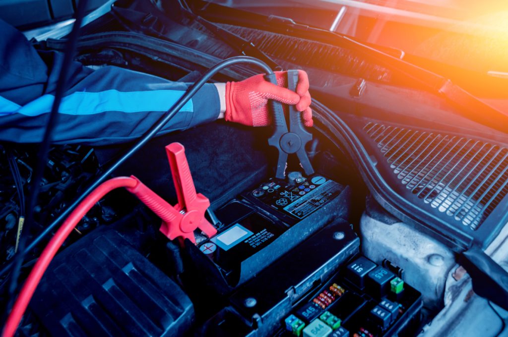 Technician jumping a car battery with jumper cables.