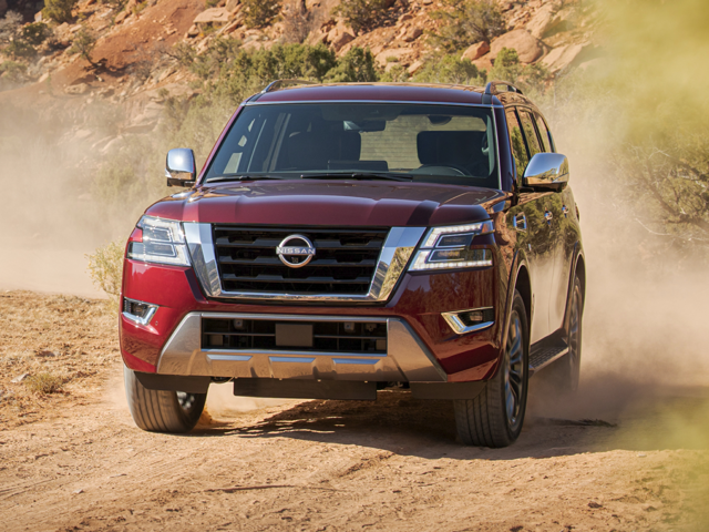 An image of a red Nissan Armada driving towards the camera over a dirt road surrounded by rocky terrain. 