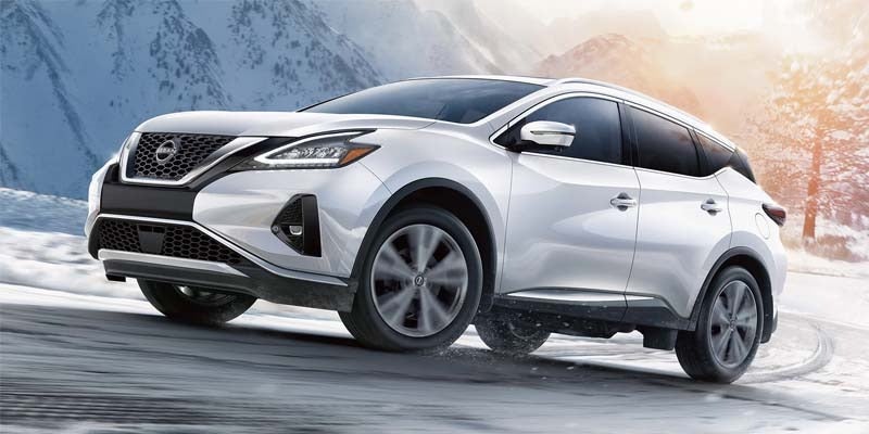 A pearl white Nissan Murano traversing a winding mountain road.