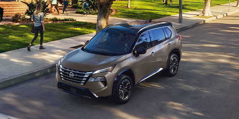 A 2024 Nissan Rogue driving down a suburban street.